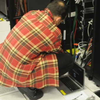 Technician working with a laptop beside server racks, representing enterprise AI retrieval infrastructure