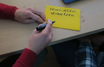 A person writes on a sticky note during a Wikimedia technical wishlist workshop, representing open source design contribution planning