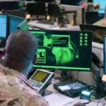 Two Air Force cyber operators work at computer monitors during a staged cyber-attack response scene