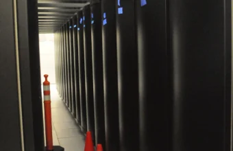 Narrow aisle behind black supercomputer racks in a data center