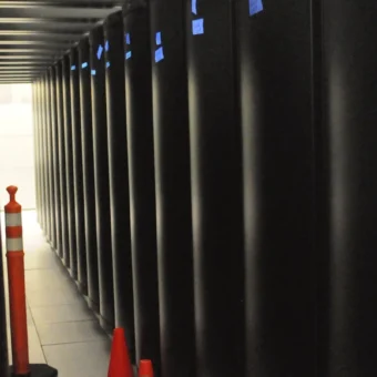 Narrow aisle behind black supercomputer racks in a data center