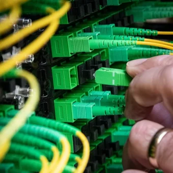 A technician connects green fiber optic cables at a data center, representing a private production inference endpoint.