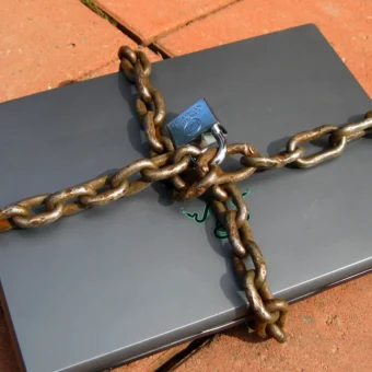 A laptop wrapped in a chain and padlock, illustrating least-privilege controls for AI agents.