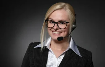 A customer-support representative wearing a headset against a dark studio background.