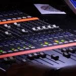 Close-up of a digital audio mixing console with many rows of sliders and channel controls