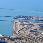 Aerial view of gantry cranes and stacked shipping containers at a container terminal, representing automated, orchestrated deployment