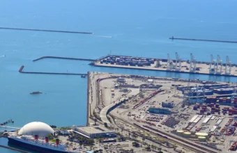 Aerial view of gantry cranes and stacked shipping containers at a container terminal, representing automated, orchestrated deployment