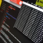 Close-up of a laptop terminal window showing scrolling log-style output beside a blurred code editor pane, illustrating raw unstructured log lines