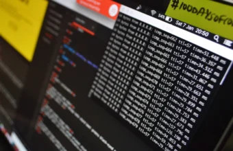 Close-up of a laptop terminal window showing scrolling log-style output beside a blurred code editor pane, illustrating raw unstructured log lines