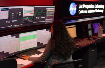 A NASA Deep Space Network operations chief monitors real-time telemetry and status dashboards across multiple screens at the Jet Propulsion Laboratory