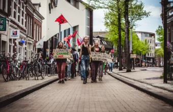 Extinction Rebellion activists march with a red XR flag and a Climate Change Is Not Cool sign through a Dutch city street