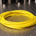 Coiled yellow fiber-optic patch cable with connectors at both ends on an optics lab bench