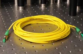 Coiled yellow fiber-optic patch cable with connectors at both ends on an optics lab bench