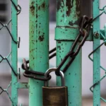 Padlock and chain securing a turquoise chain-link gate, representing an authentication bypass in self-hosted Git infrastructure