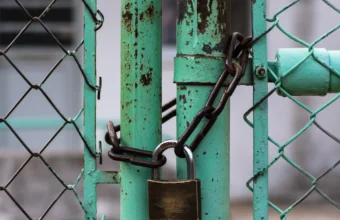 Padlock and chain securing a turquoise chain-link gate, representing an authentication bypass in self-hosted Git infrastructure
