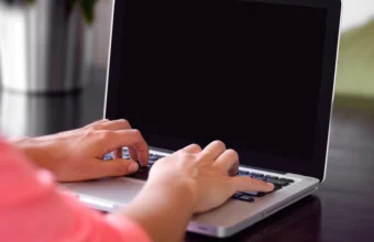Close-up of two hands typing on a laptop keyboard with a dark blank screen