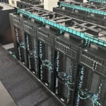 Rows of liquid-cooled supercomputer server racks with turquoise cable management at the Barcelona Supercomputing Center, representing the GPU infrastructure that LLM serving benchmarks measure