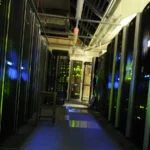 A dimly lit data center aisle with tall server racks showing blue and green status lights on both sides