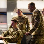 Military cyber operators monitor screens at workstations, illustrating cyber defense operations