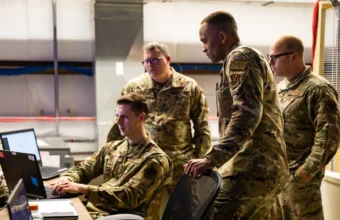 Military cyber operators monitor screens at workstations, illustrating cyber defense operations