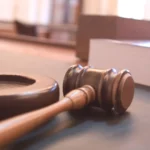 A wooden judge's gavel resting on its sound block in a courtroom, representing an LLM acting as an automated judge that grades an AI agent's answers