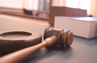 A wooden judge's gavel resting on its sound block in a courtroom, representing an LLM acting as an automated judge that grades an AI agent's answers