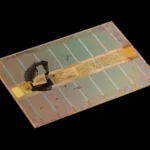 Macro photograph of an HBM DRAM memory die from an AMD Radeon RX Vega 64 graphics card, showing the dense grid of through-silicon-via contact points on the stacked memory die