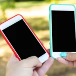 Two hands hold up smartphones with blank screens toward each other outdoors