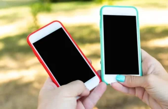 Two hands hold up smartphones with blank screens toward each other outdoors
