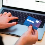 A person holds a bank card next to an open laptop showing an online checkout page, illustrating digital payments