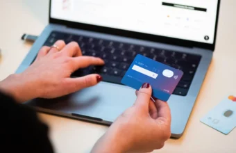 A person holds a bank card next to an open laptop showing an online checkout page, illustrating digital payments