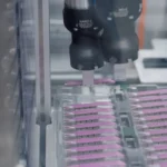 A robotic gripper arm picks parts from a tray on a manufacturing line, representing how an AI agent calls the specific tool it needs to complete a task