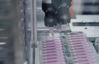 A robotic gripper arm picks parts from a tray on a manufacturing line, representing how an AI agent calls the specific tool it needs to complete a task