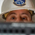 A U.S. Air Force communications technician peers over network rack equipment, representing the ongoing oversight AI agent connectors require as their permissions and tools change over time