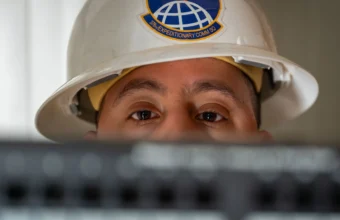 A U.S. Air Force communications technician peers over network rack equipment, representing the ongoing oversight AI agent connectors require as their permissions and tools change over time