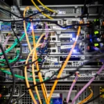 Close-up of colorful network and power cables tangled behind a rack of servers, with blue and green status LEDs