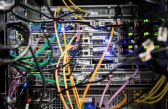 Close-up of colorful network and power cables tangled behind a rack of servers, with blue and green status LEDs