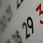 Close-up photo of a wall calendar showing the 29th and 30th, with the 30th highlighted in red, shot at a shallow depth of field