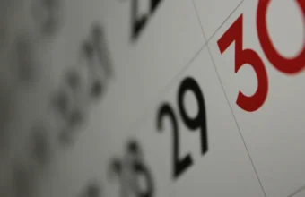 Close-up photo of a wall calendar showing the 29th and 30th, with the 30th highlighted in red, shot at a shallow depth of field
