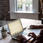 Close-up of a developer typing on a laptop at a wooden desk