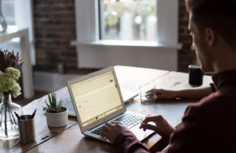 Close-up of a developer typing on a laptop at a wooden desk
