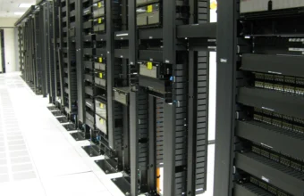 A data center aisle showing a long row of rack-mounted network switches, patch panels, and cabling