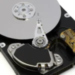 An open 3.5 inch hard disk drive with the top cover removed, showing the spinning platter, read/write head, and actuator arm
