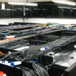 Overhead cable trays and rack-mounted servers in a data center, representing the infrastructure behind Models-as-a-Service governance