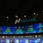 Nasdaq MarketSite video screens displaying the Nasdaq logo and stock ticker data above a Times Square TV studio