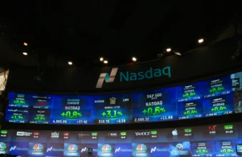 Nasdaq MarketSite video screens displaying the Nasdaq logo and stock ticker data above a Times Square TV studio