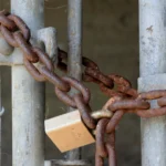 A rusty chain and padlock secured through a metal gate, representing access control