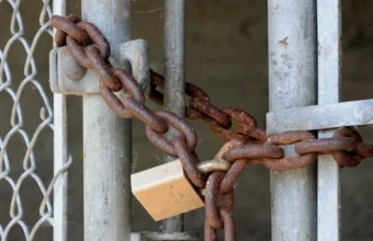 A rusty chain and padlock secured through a metal gate, representing access control