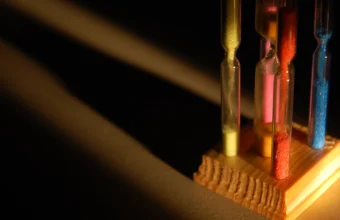 Four colorful hourglasses in a light beam, illustrating how a dependency cooldown makes package managers wait before trusting a new release