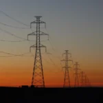 Electricity transmission towers silhouetted against a sunset, representing the power grid strain behind New York data center policy